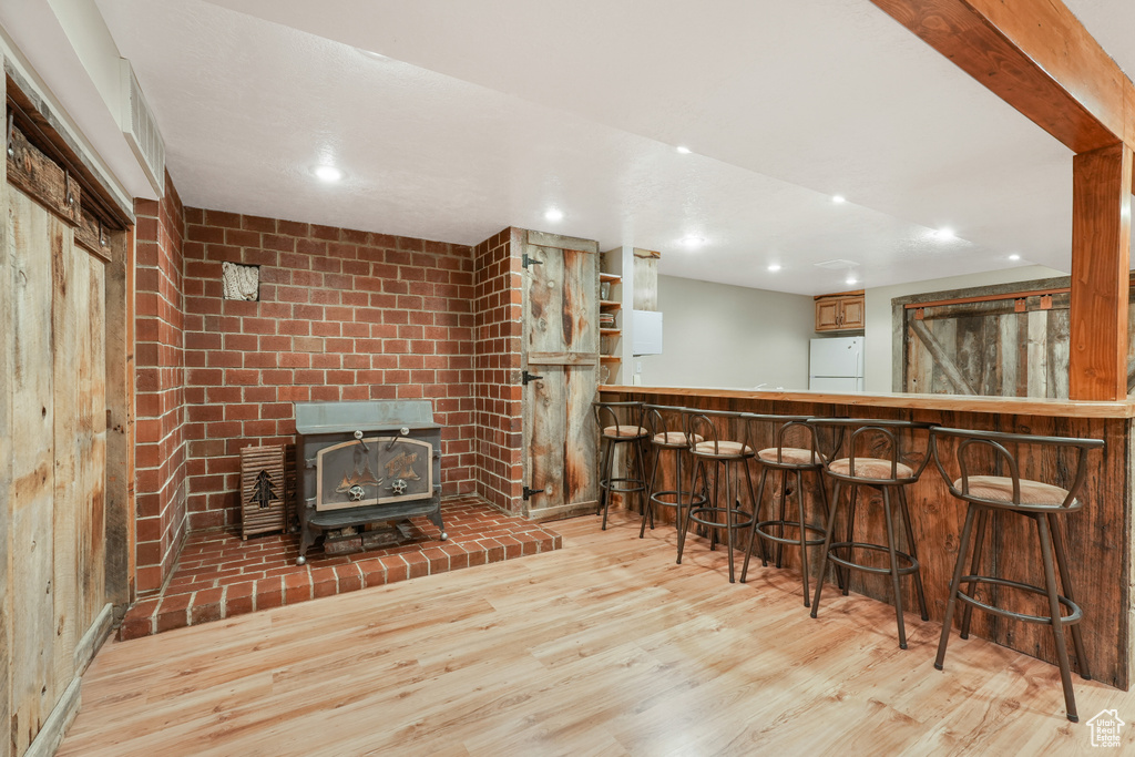 Bar with a wood stove, white refrigerator, and light wood-type flooring