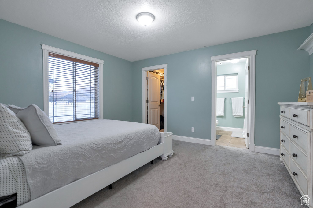 Bedroom with connected bathroom, light colored carpet, a spacious closet, a textured ceiling, and a closet