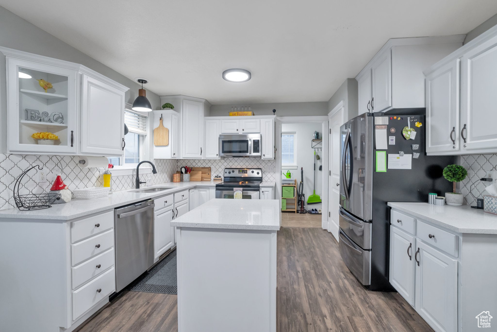 Kitchen featuring dark wood-type flooring, appliances with stainless steel finishes, white cabinetry, a center island, and hanging light fixtures