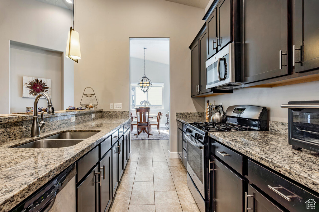 Kitchen featuring decorative light fixtures, appliances with stainless steel finishes, light stone counters, light tile floors, and sink