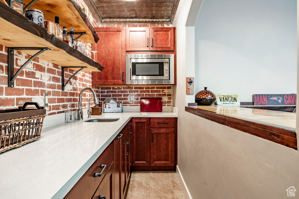 Kitchen featuring stainless steel microwave, brick wall, sink, and light tile floors