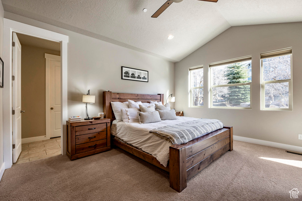 Bedroom featuring ceiling fan, light carpet, vaulted ceiling, and a textured ceiling