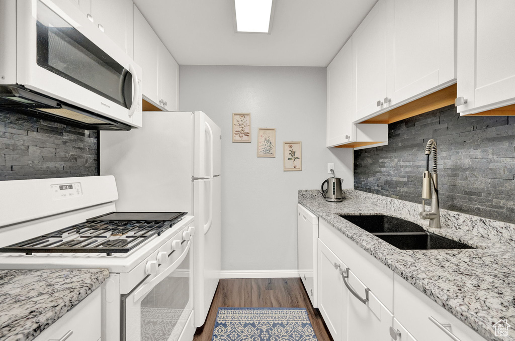 Kitchen with light stone countertops, white appliances, tasteful backsplash, and dark wood-type flooring