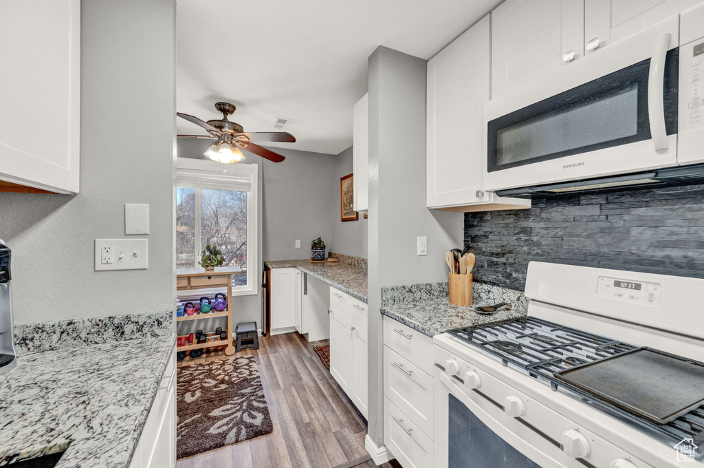 Kitchen featuring tasteful backsplash, light stone counters, ceiling fan, white appliances, and hardwood / wood-style flooring