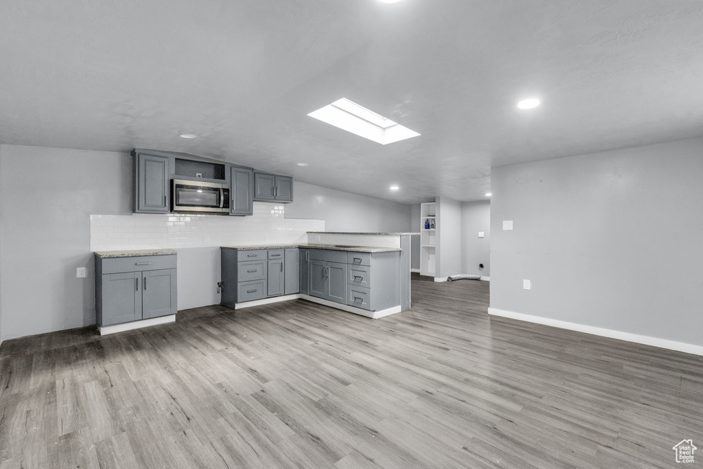 Kitchen featuring lofted ceiling with skylight, gray cabinetry, backsplash, and light hardwood / wood-style floors