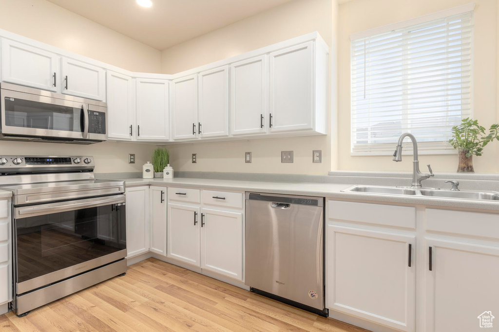 Kitchen with appliances with stainless steel finishes, light hardwood / wood-style flooring, and white cabinetry