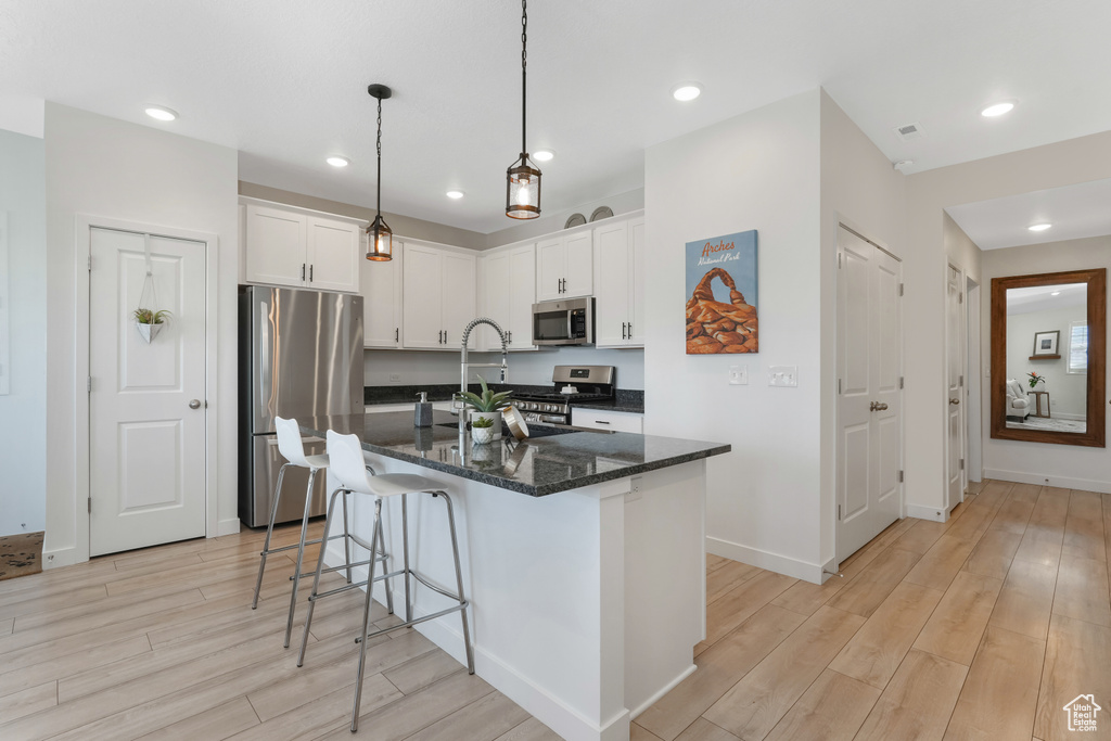 Kitchen featuring white cabinets, hanging light fixtures, light hardwood / wood-style floors, and appliances with stainless steel finishes
