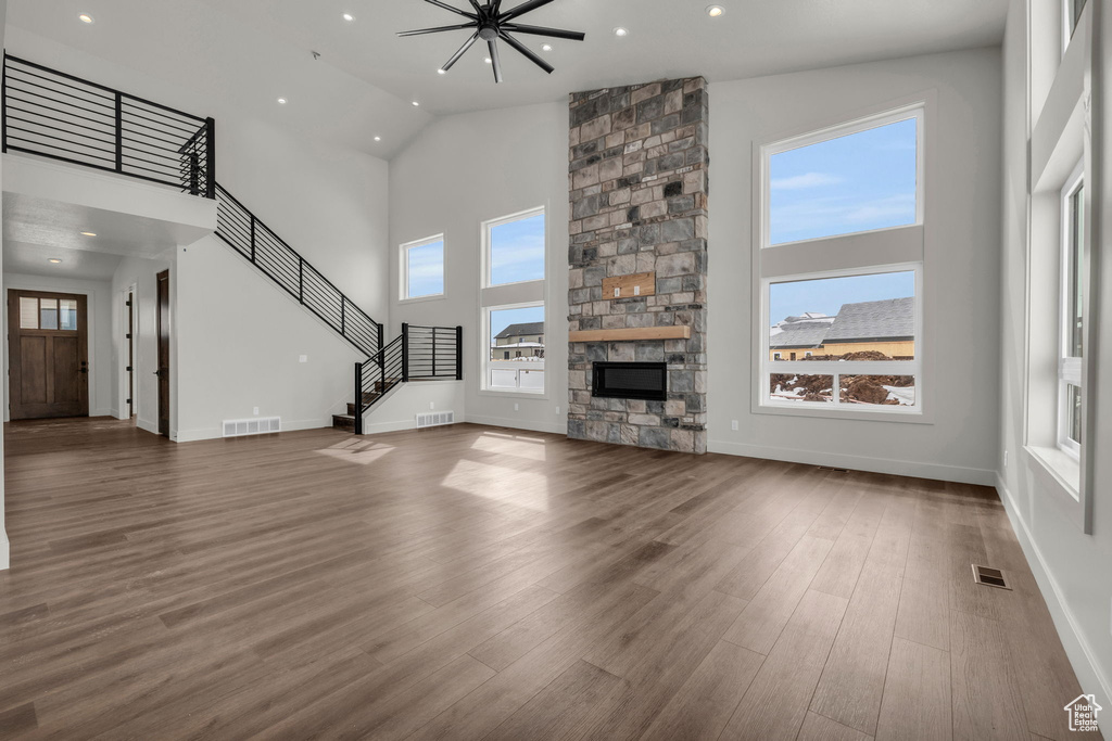 Unfurnished living room with a high ceiling, a stone fireplace, and dark hardwood / wood-style flooring