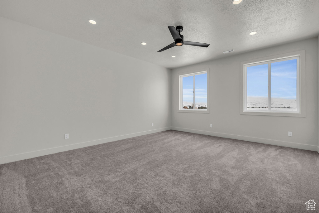 Empty room featuring light carpet, ceiling fan, and a textured ceiling