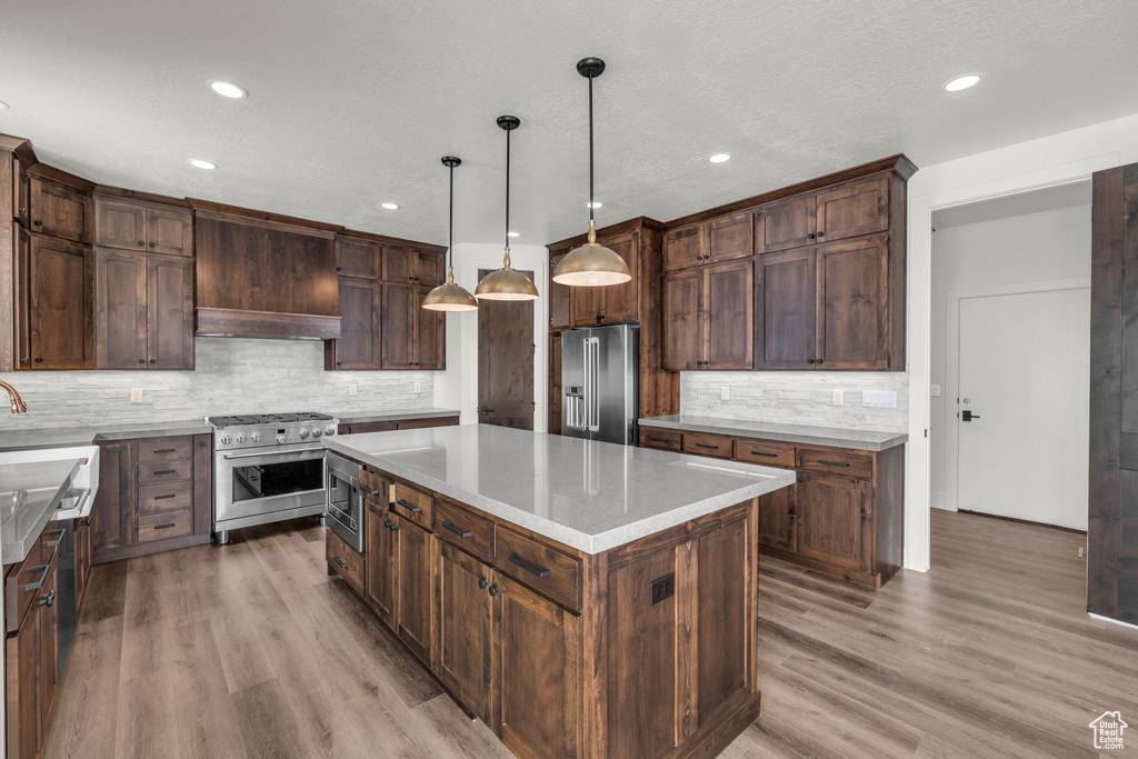 Kitchen with a kitchen island, backsplash, light hardwood / wood-style floors, decorative light fixtures, and high quality appliances