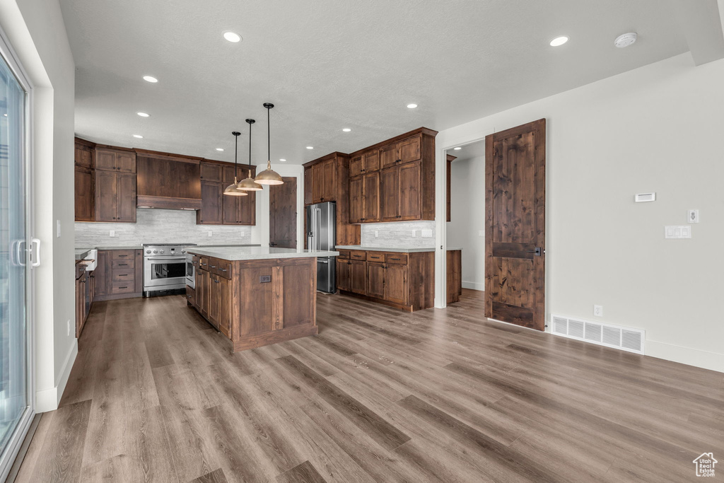 Kitchen with hanging light fixtures, backsplash, premium range hood, light hardwood / wood-style flooring, and a kitchen island
