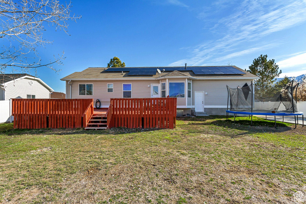 Rear view of house with a yard, solar panels, a trampoline, and a wooden deck
