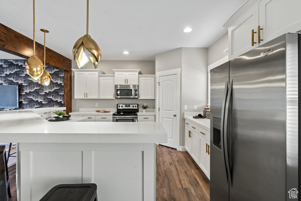 Kitchen with pendant lighting, stainless steel appliances, a breakfast bar area, white cabinets, and dark hardwood / wood-style flooring