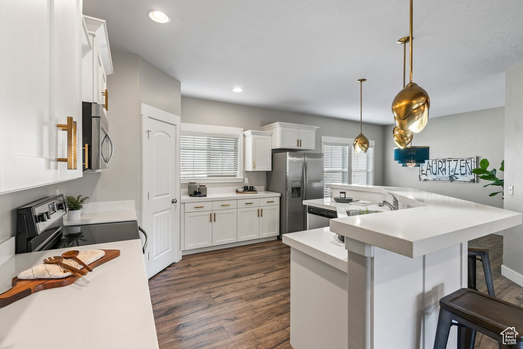 Kitchen featuring appliances with stainless steel finishes, hanging light fixtures, dark wood-type flooring, a kitchen bar, and white cabinets