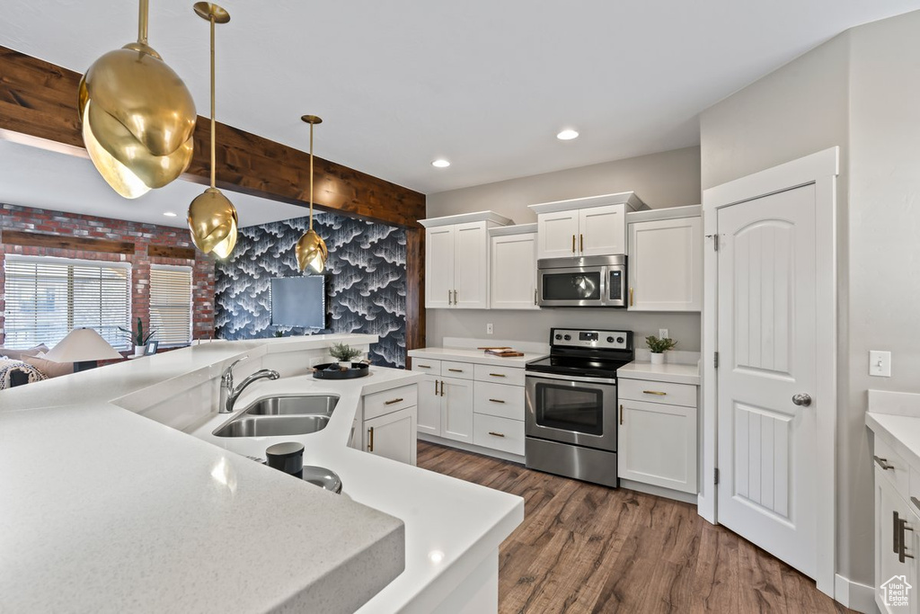 Kitchen featuring decorative light fixtures, white cabinetry, dark wood-type flooring, appliances with stainless steel finishes, and sink