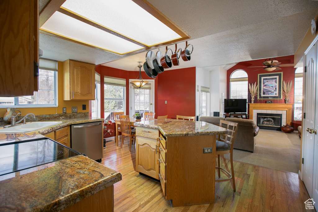 Kitchen featuring a tiled fireplace, ceiling fan, a center island, light wood-type flooring, and dishwasher