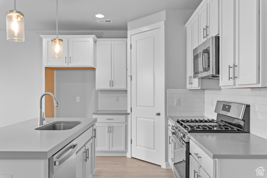 Kitchen featuring pendant lighting, appliances with stainless steel finishes, tasteful backsplash, white cabinetry, and light wood-type flooring