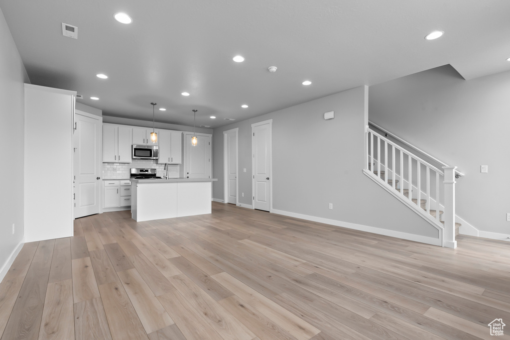 Kitchen with pendant lighting, tasteful backsplash, light hardwood / wood-style floors, white cabinetry, and a kitchen island with sink