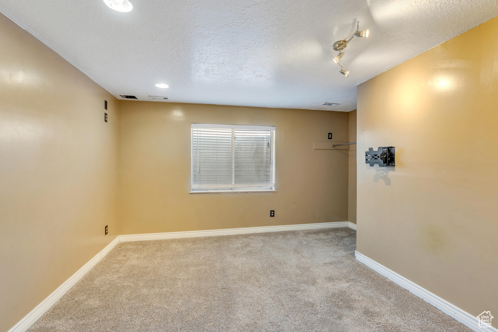 Carpeted empty room with a textured ceiling and rail lighting