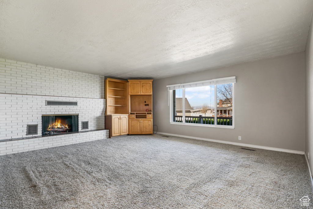 Unfurnished living room with light carpet, a fireplace, and brick wall