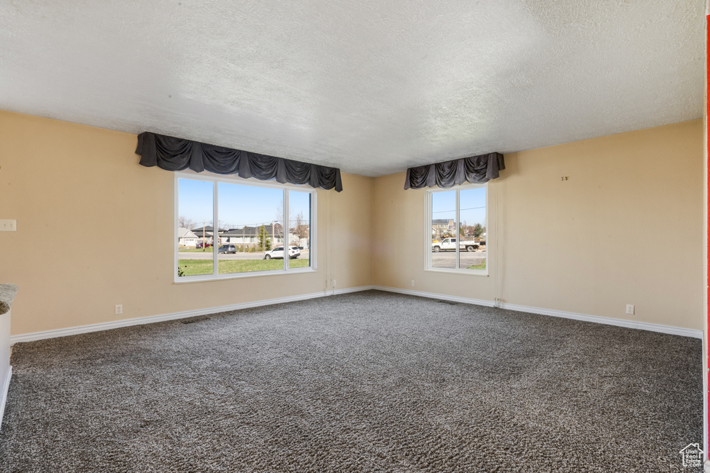 Empty room featuring plenty of natural light, dark colored carpet, and a textured ceiling