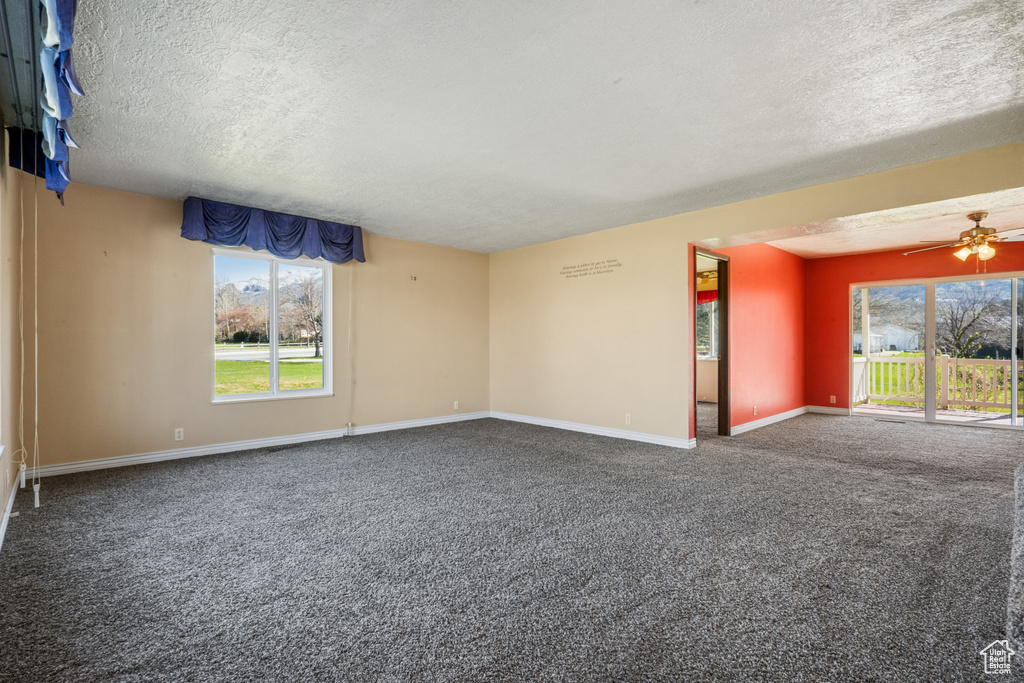 Carpeted empty room featuring plenty of natural light, a textured ceiling, and ceiling fan