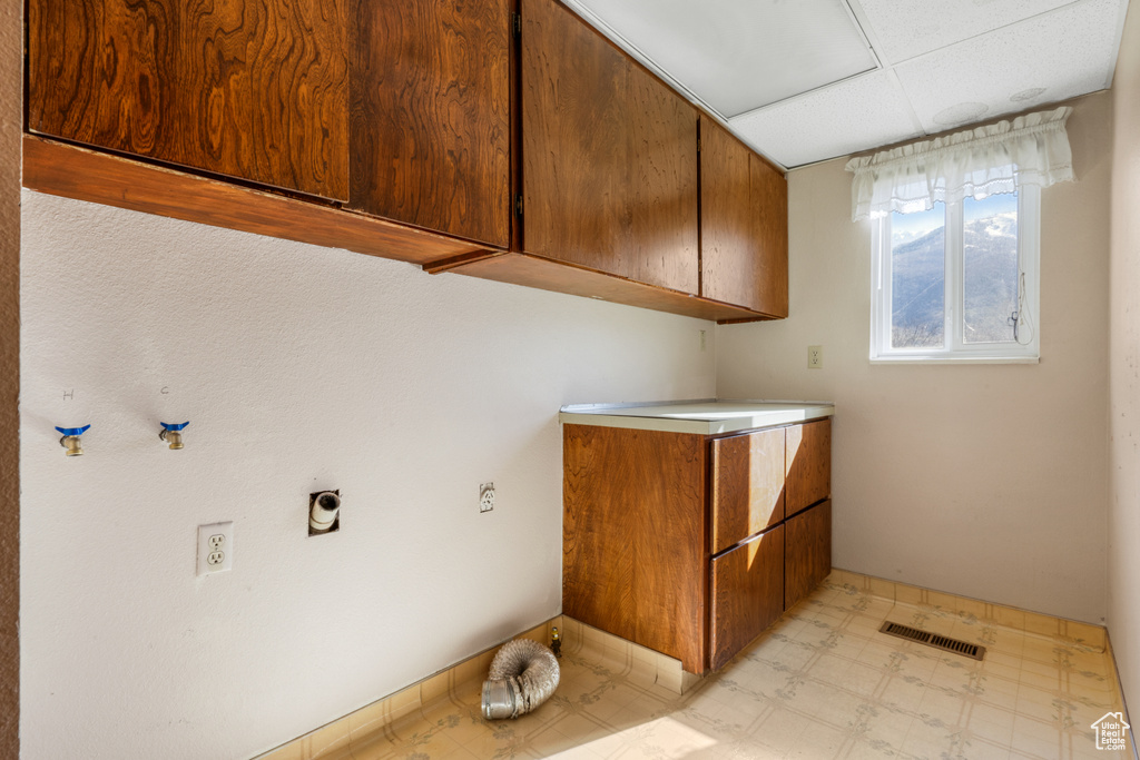 Laundry room featuring electric dryer hookup, cabinets, and light tile flooring