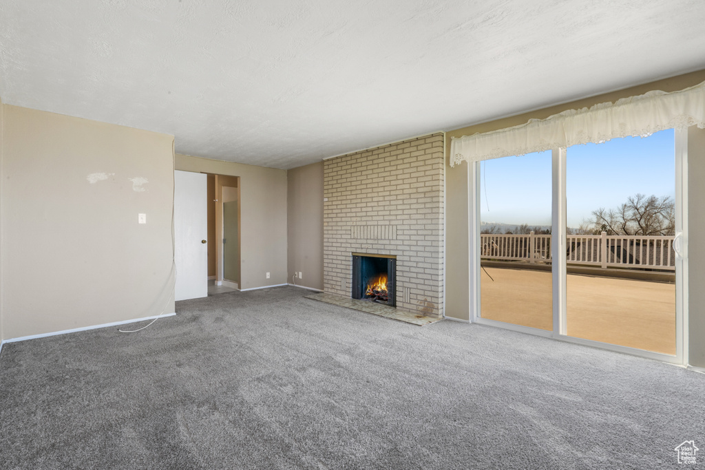 Unfurnished living room with brick wall, carpet flooring, and a fireplace