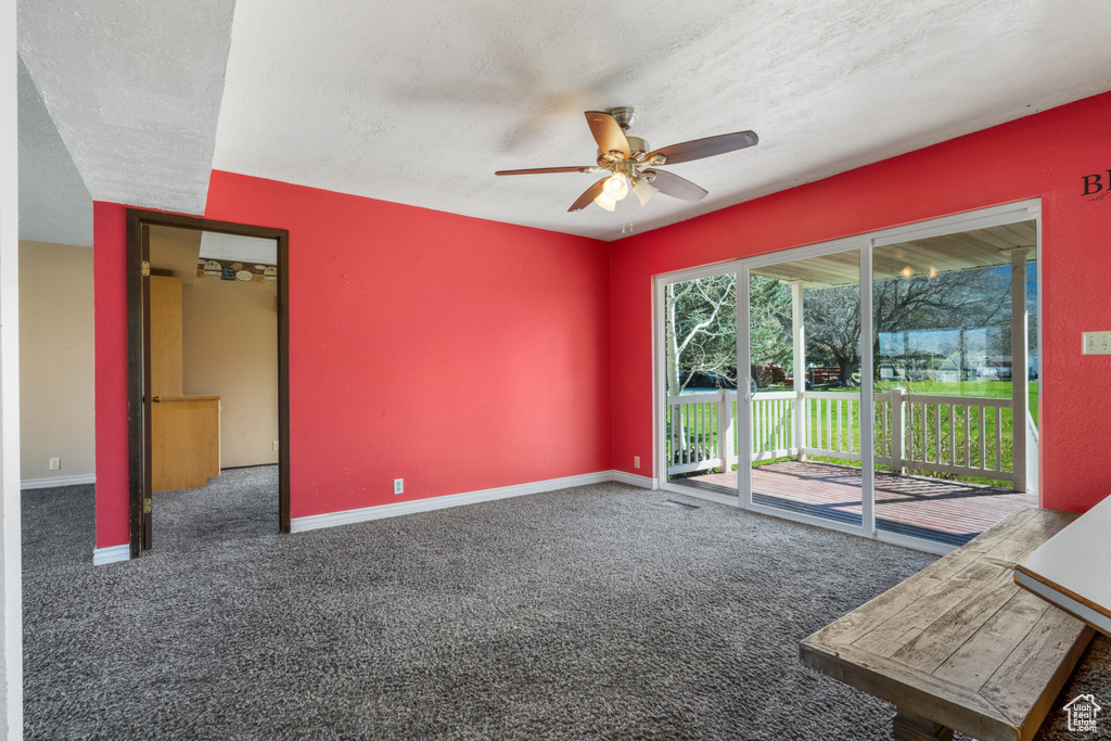 Unfurnished room featuring dark carpet, ceiling fan, and a textured ceiling
