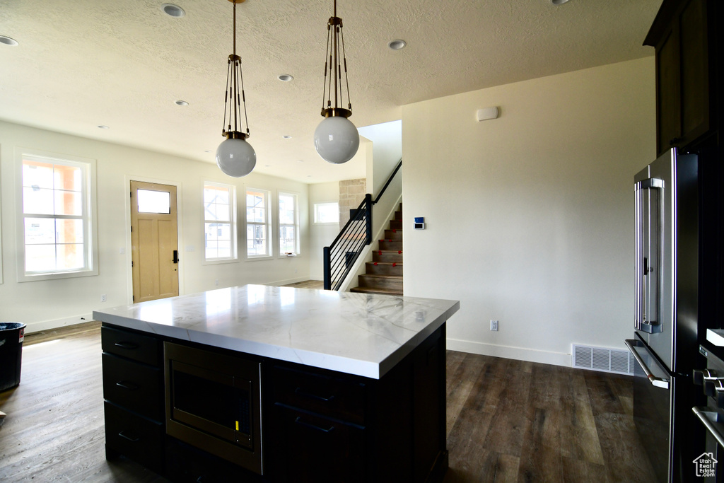 Kitchen featuring a center island, black microwave, decorative light fixtures, high end refrigerator, and dark hardwood / wood-style floors