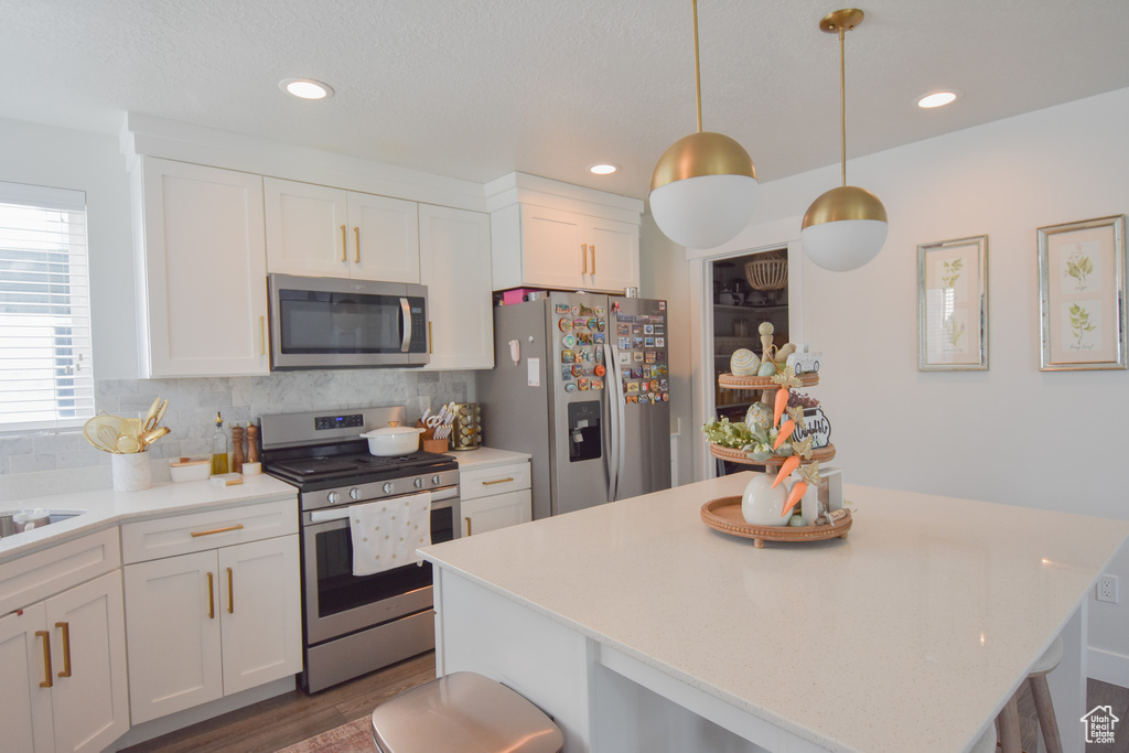 Kitchen featuring pendant lighting, stainless steel appliances, tasteful backsplash, white cabinetry, and dark hardwood / wood-style flooring
