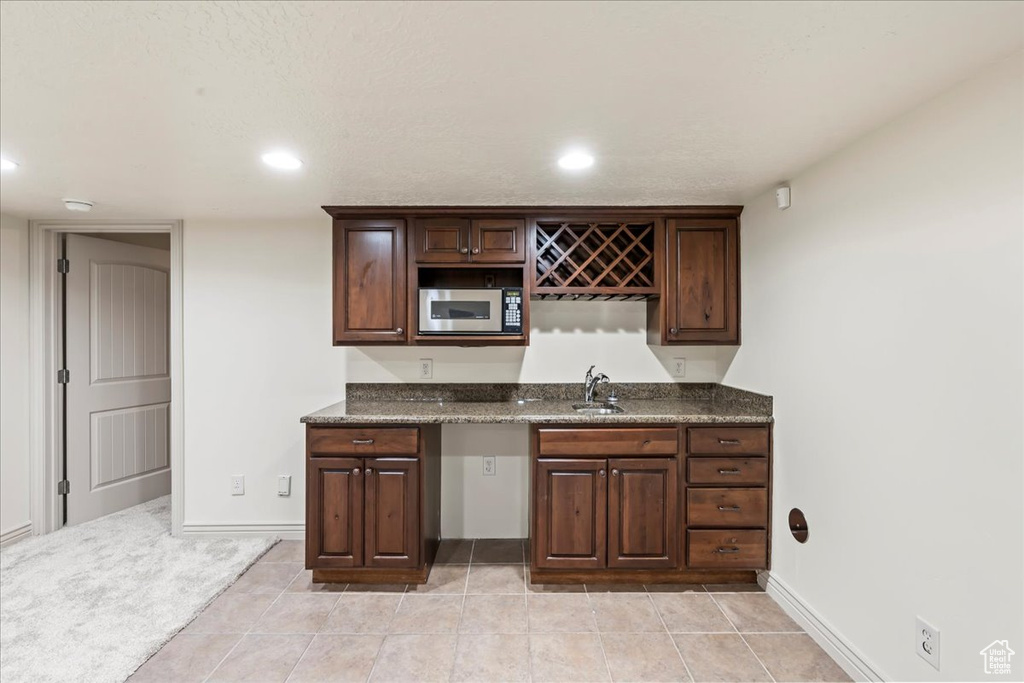Bar featuring light tile flooring, dark brown cabinetry, black microwave, and sink