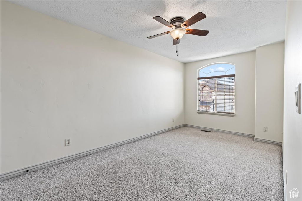 Empty room with light carpet, a textured ceiling, and ceiling fan