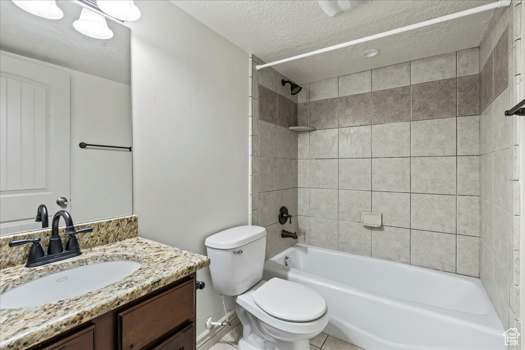 Full bathroom featuring toilet, tiled shower / bath, vanity, a textured ceiling, and tile floors