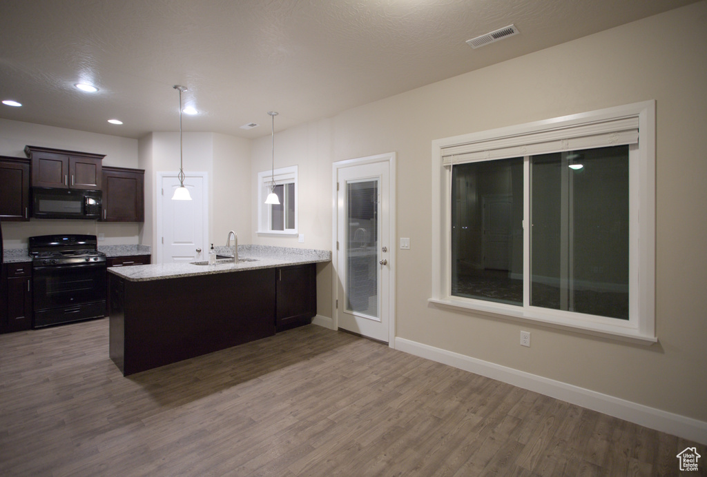Kitchen with hanging light fixtures, kitchen peninsula, hardwood / wood-style flooring, and black appliances