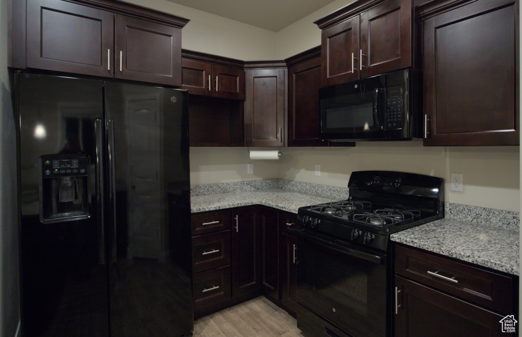 Kitchen with light stone counters, dark brown cabinets, light wood-type flooring, and black appliances