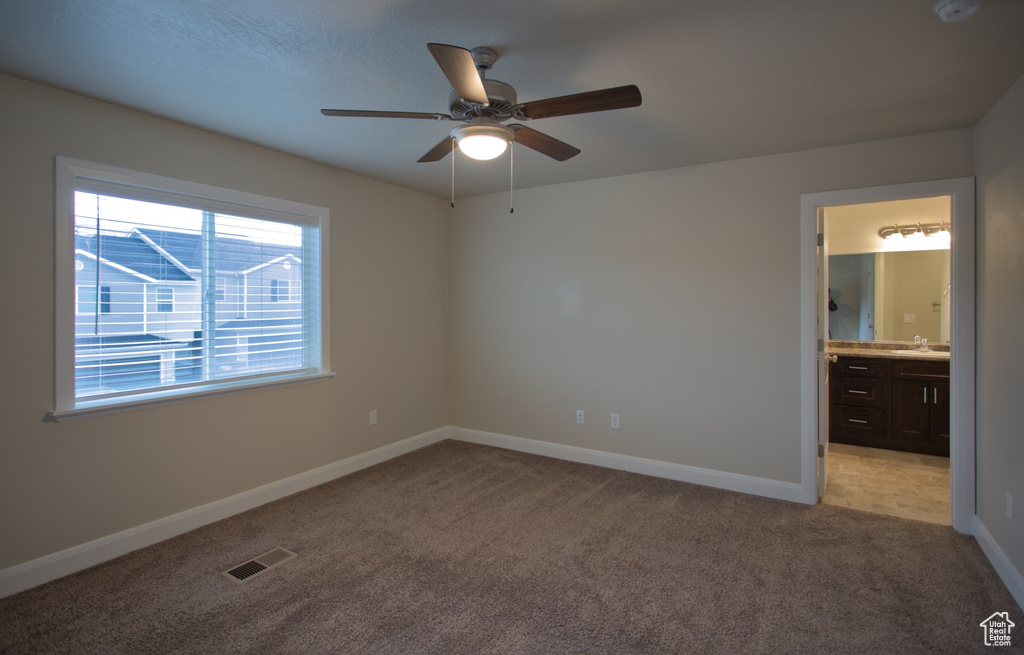Unfurnished bedroom with ceiling fan, ensuite bathroom, and light colored carpet