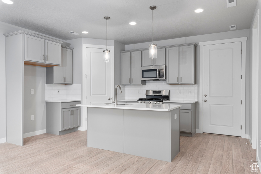 Kitchen featuring an island with sink, stainless steel appliances, gray cabinets, light wood-type flooring, and sink
