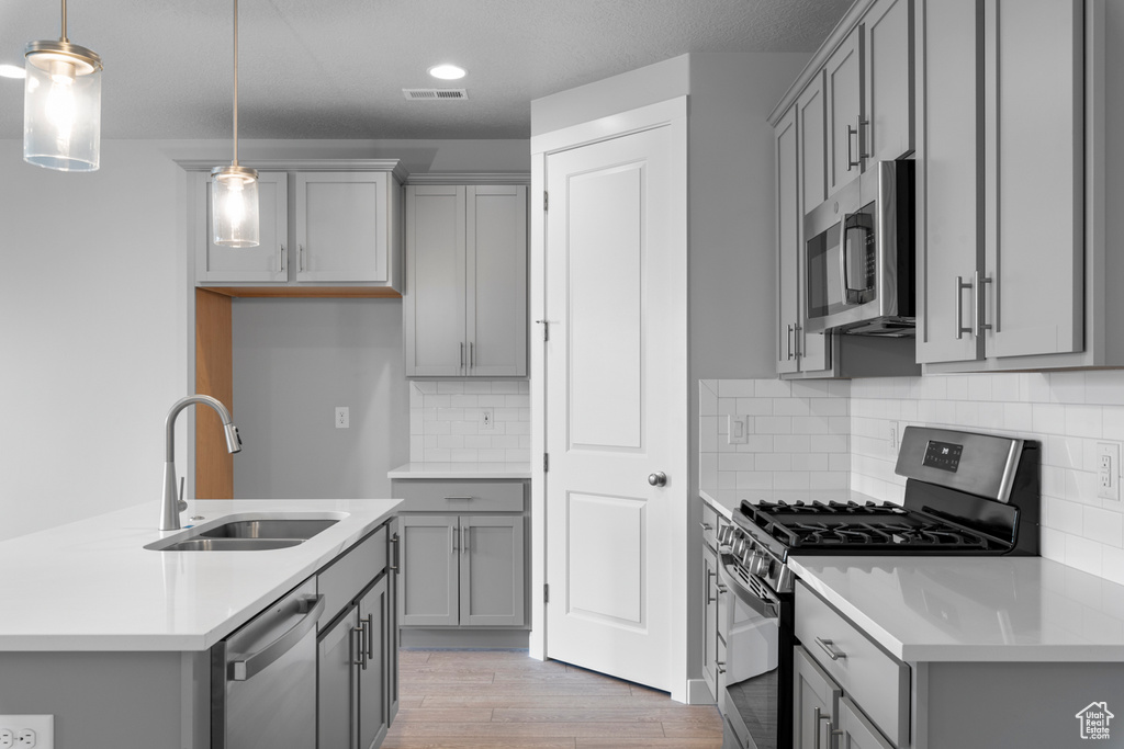 Kitchen featuring backsplash, stainless steel appliances, decorative light fixtures, and light wood-type flooring