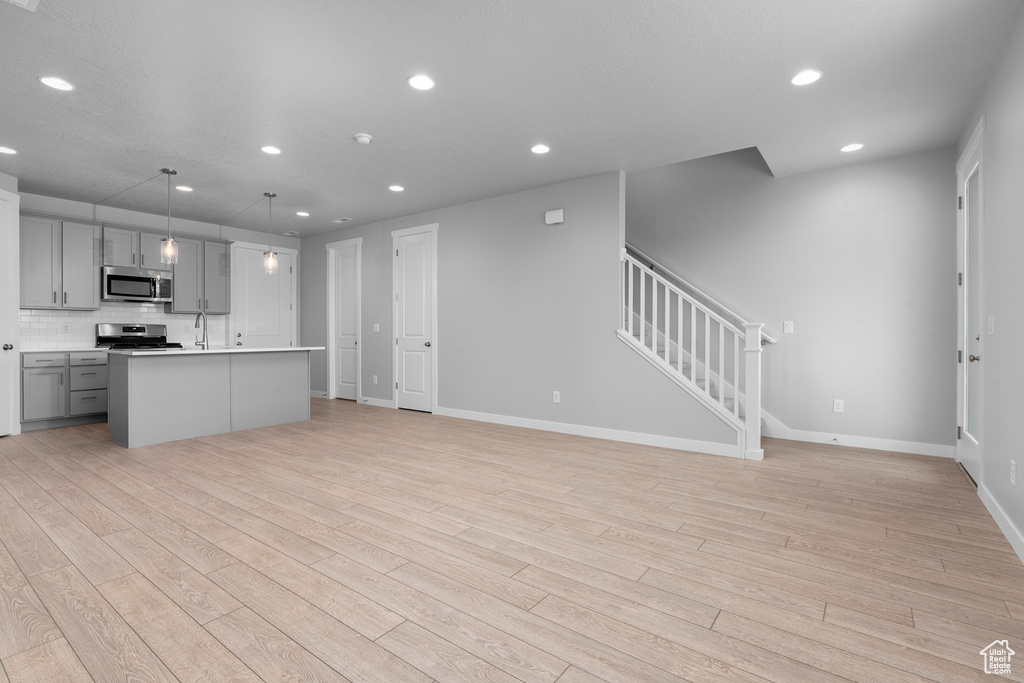 Kitchen with light hardwood / wood-style floors, stove, tasteful backsplash, gray cabinets, and pendant lighting