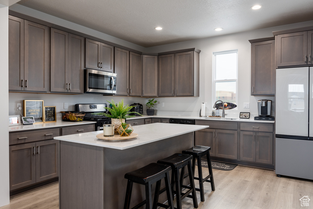 Kitchen featuring light hardwood / wood-style floors, a center island, a breakfast bar area, appliances with stainless steel finishes, and sink