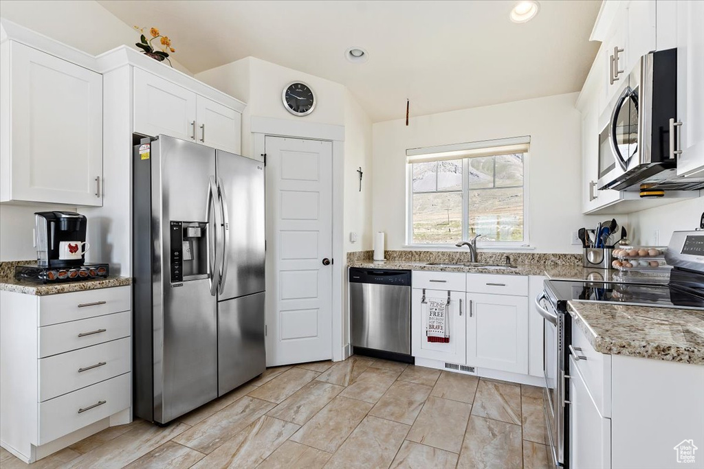 Kitchen featuring stainless steel appliances, white cabinets, light stone countertops, and sink