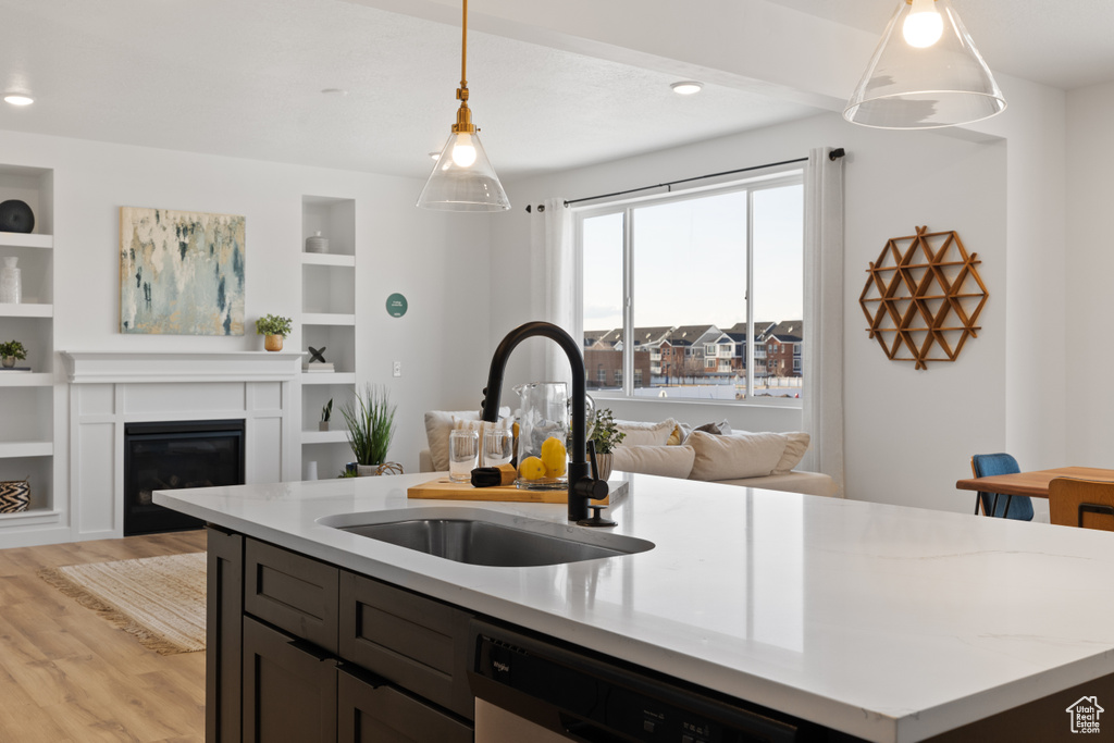 Kitchen with light stone countertops, dishwashing machine, light hardwood / wood-style floors, sink, and pendant lighting