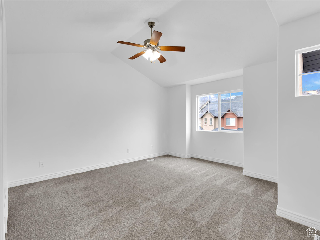 Empty room with lofted ceiling, light carpet, and ceiling fan