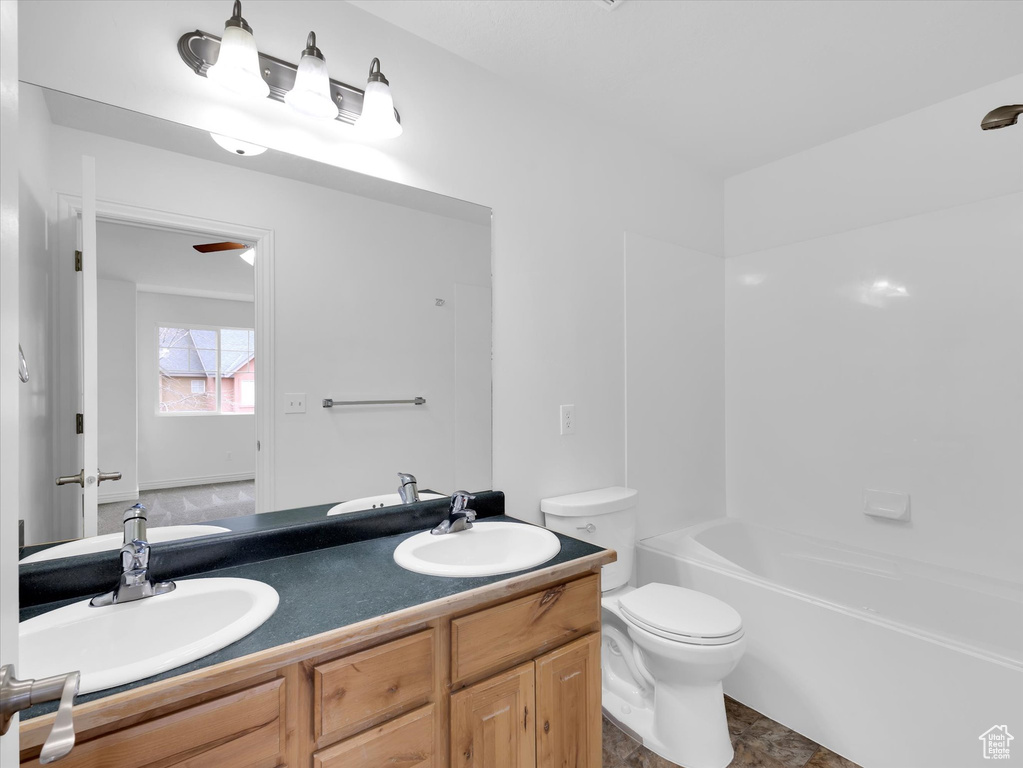 Full bathroom with toilet, vanity with extensive cabinet space, tub / shower combination, dual sinks, and tile flooring