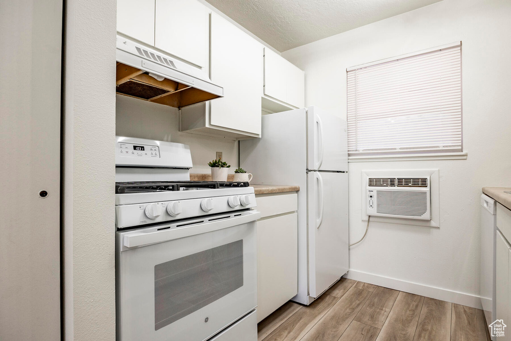 Kitchen with white cabinets, premium range hood, light hardwood / wood-style floors, and white appliances