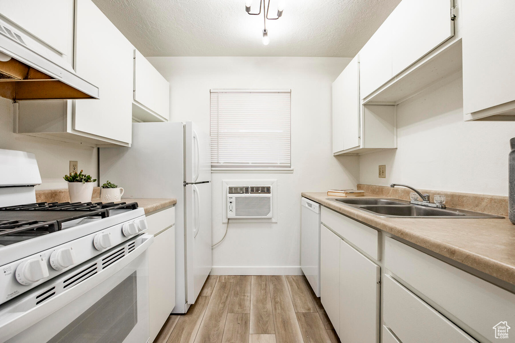 Kitchen with white appliances, sink, white cabinets, light hardwood / wood-style floors, and premium range hood