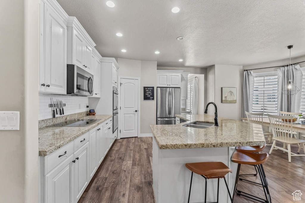 Kitchen with white cabinetry, dark wood-type flooring, appliances with stainless steel finishes, sink, and pendant lighting