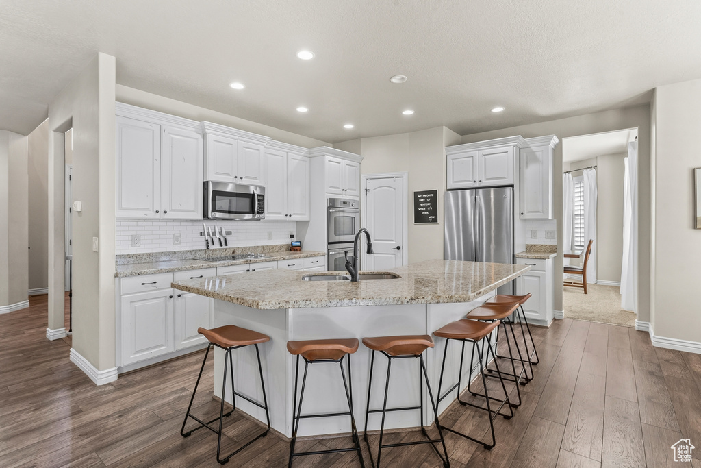 Kitchen with an island with sink, sink, hardwood / wood-style floors, white cabinets, and stainless steel appliances