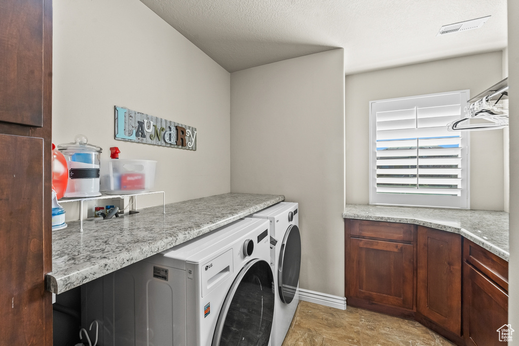 Washroom featuring a textured ceiling, washer and dryer, and light tile floors